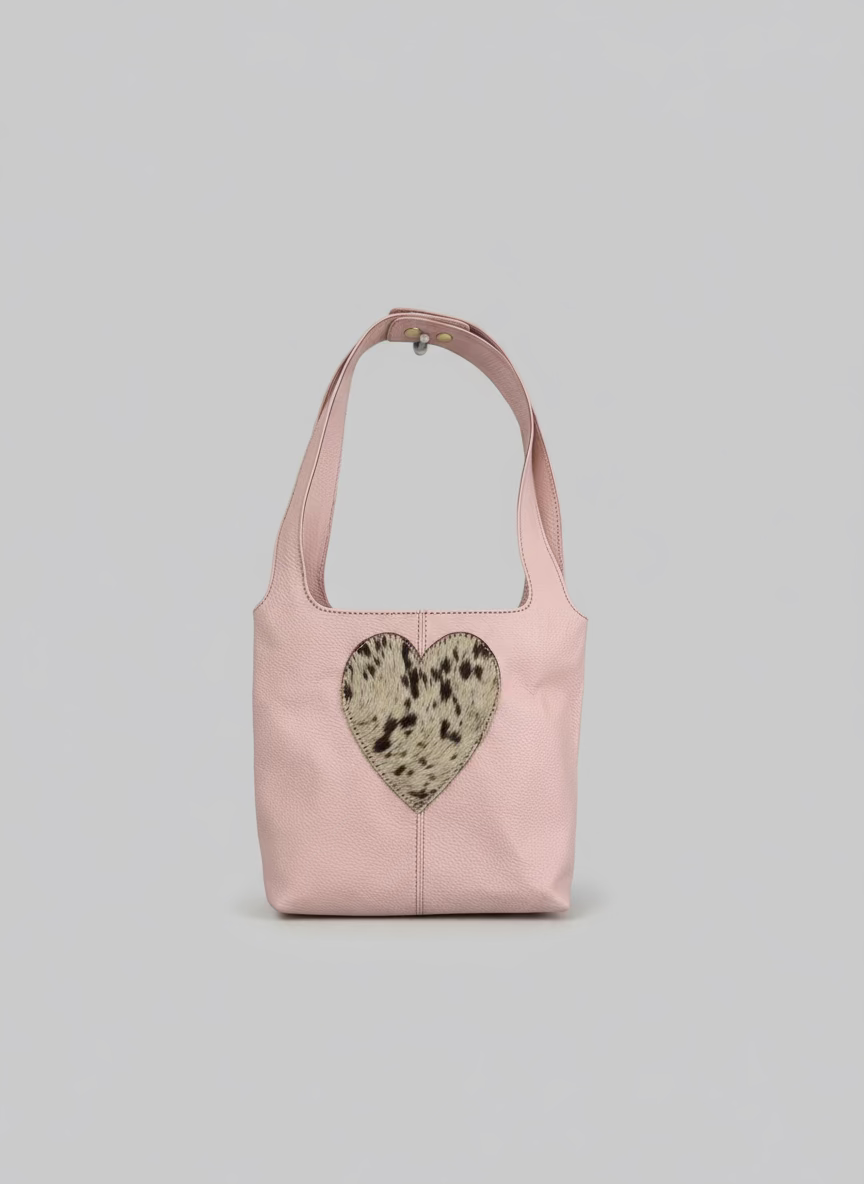 Pink handbag with a heart-shaped cutout featuring a spotted pattern, hanging on a white柱子.