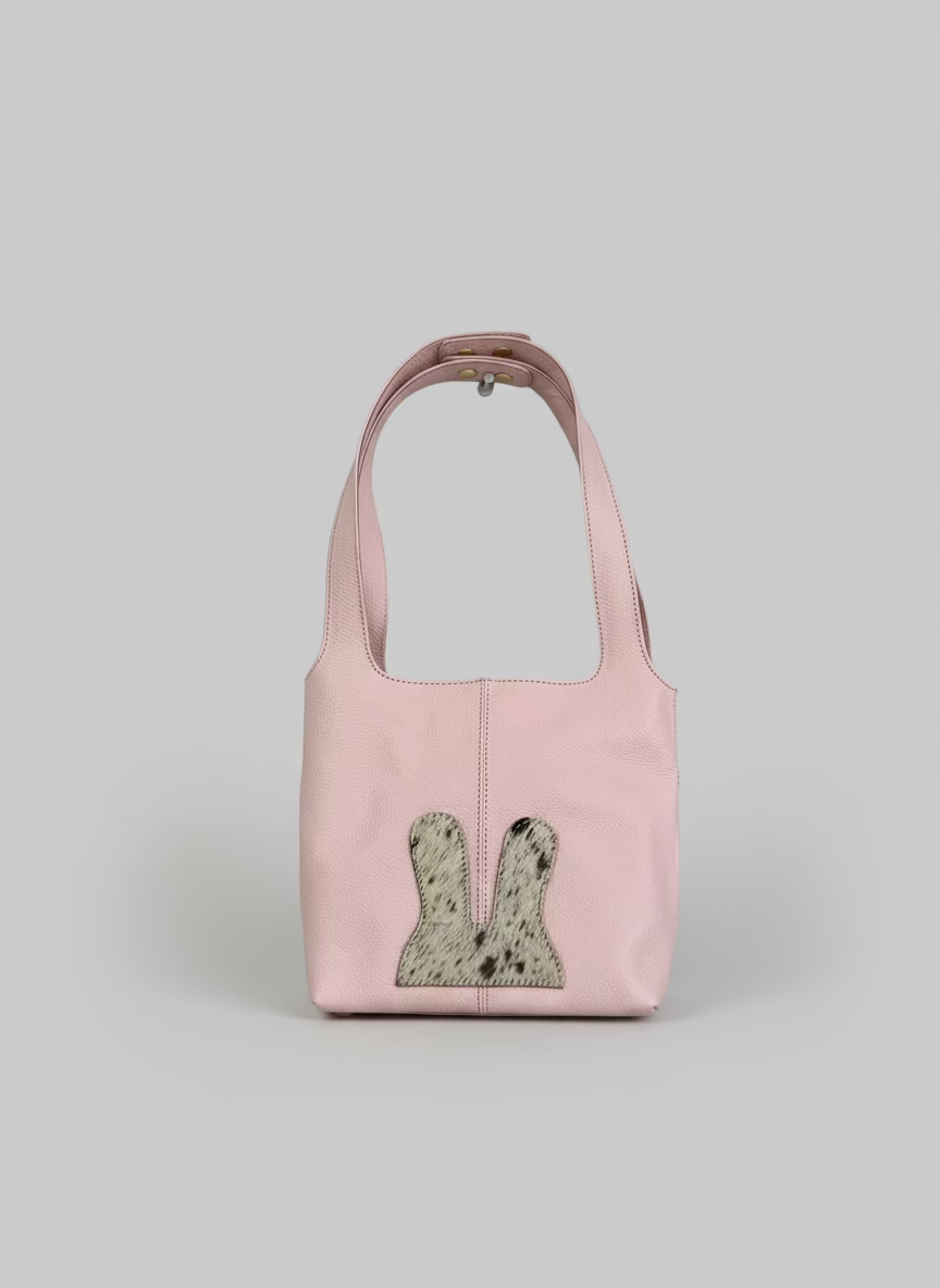 Pink handbag with a textured patch hanging on a white wall.